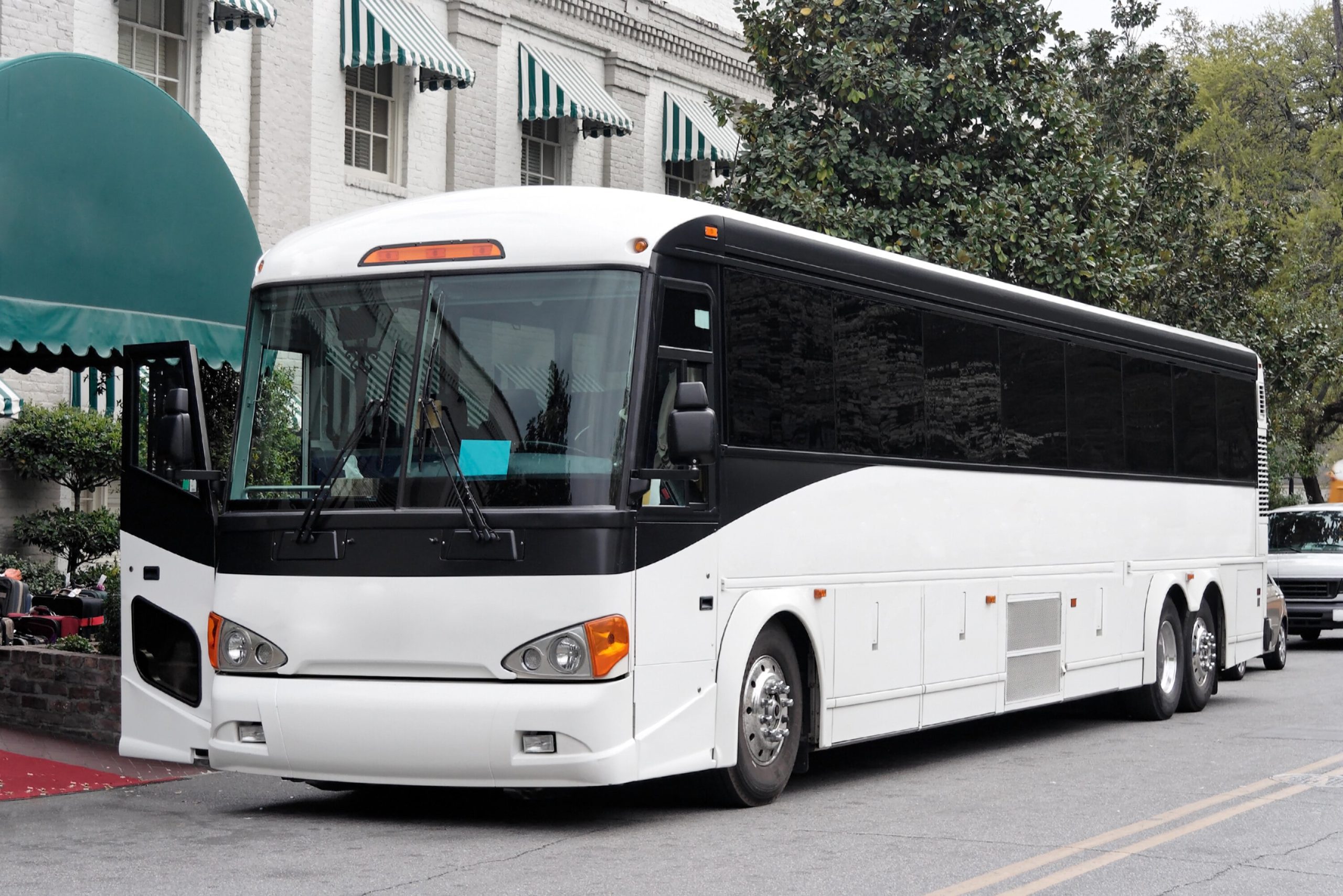 A white charter bus parked outside of a hotel that has a green awning.
